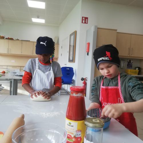Zwei Schüler knetet teig, einer reibt Käse