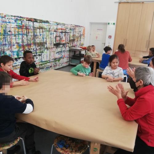 Kinder sitzen um einen Tisch mit der kreativen Leitung