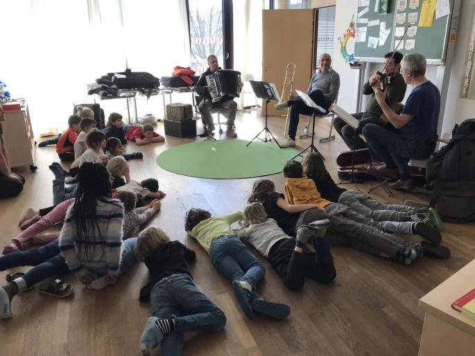Kinder im Sitzkreis hören Musiker:innen zu
